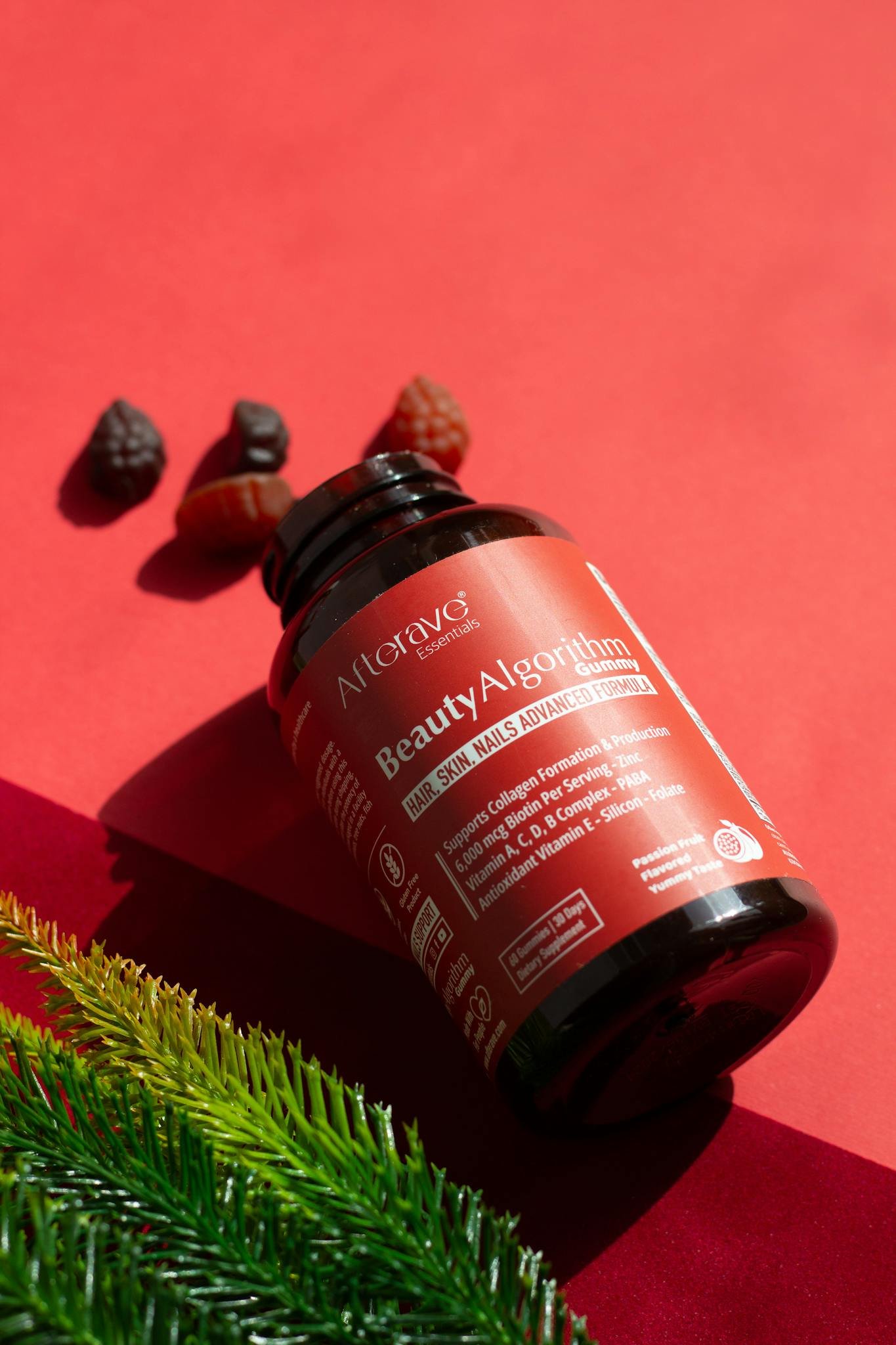 A bottle of beauty gummies on a red surface with pine leaves and berries, ideal for hair, skin, and nails.