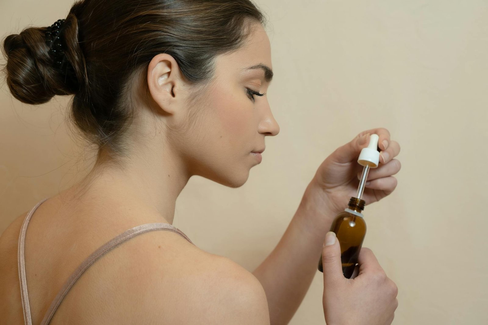 Caucasian woman using a dropper to apply essential oil, highlighting self-care and skincare routines.